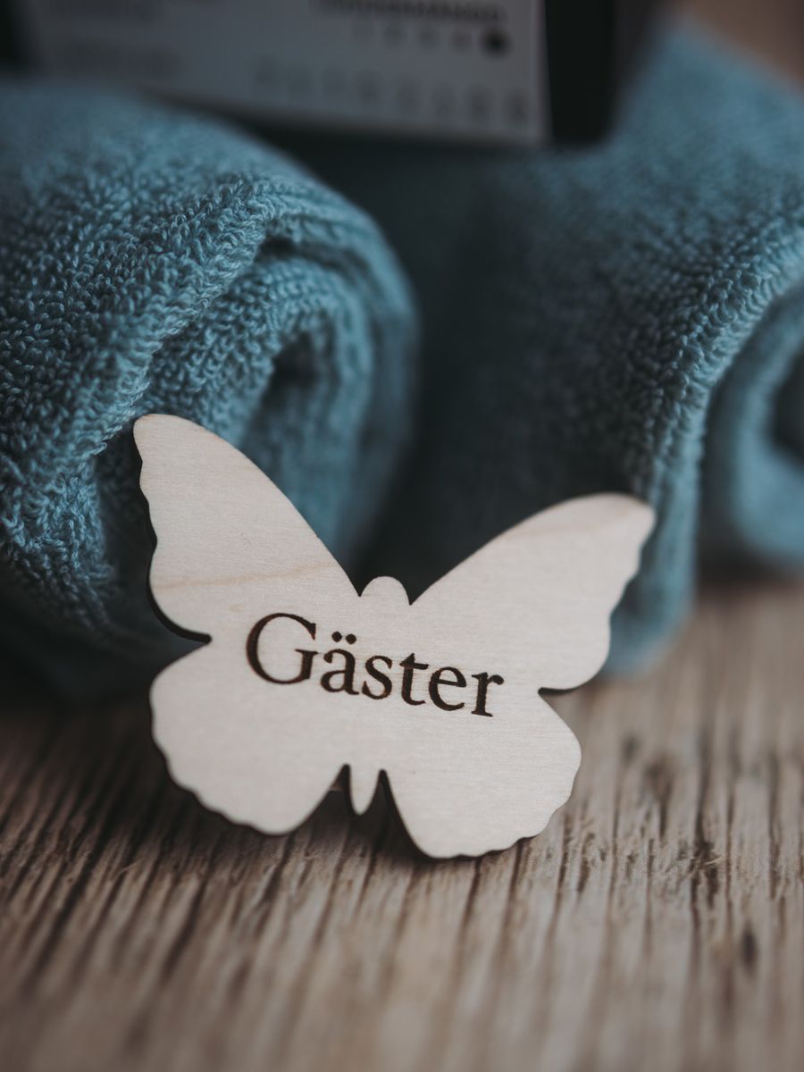 fjäril med ordet gäster ingraverat. Träskylt som monteras på gästhandduken med magnet