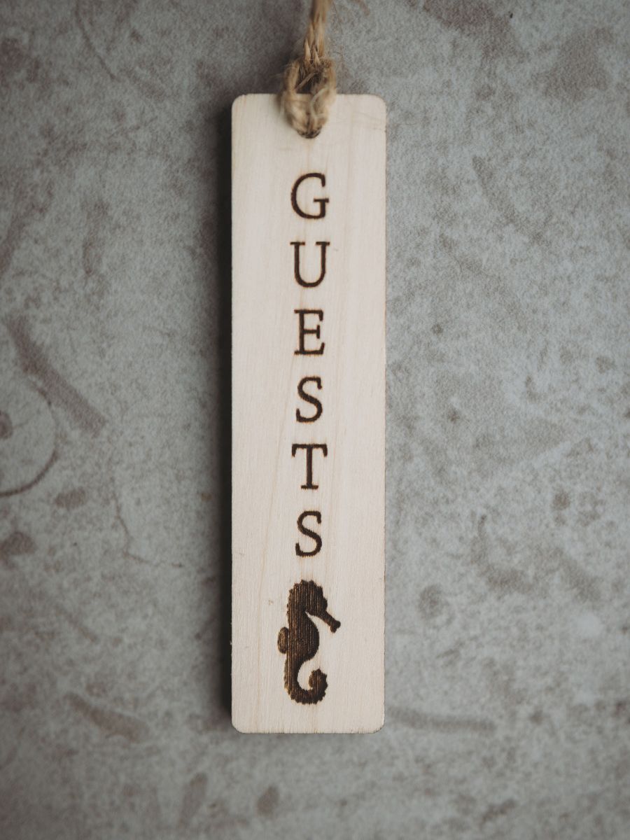 graverad sjöhäst och ordet Guests på skylt i ekfaner. Monteras på gästhandduken