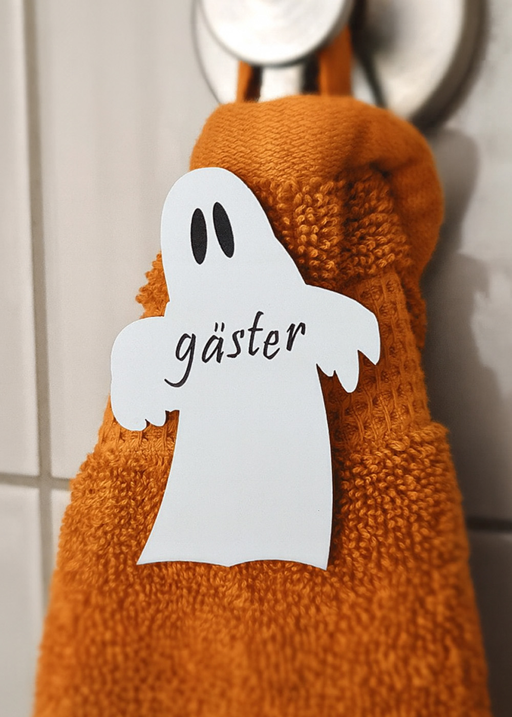 vitt spöke med texten gäster ingraverat i svart. Sitter på orange gästhandduk. Hygienisk och dekorativt till Halloween