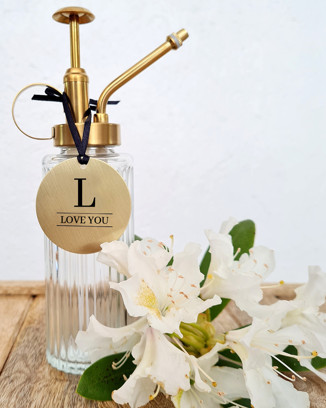 skylt i mässing, graverad text och versal love you vita blommor och sprayflaska